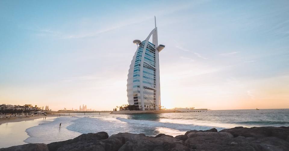 Burj Al Arab sail-shaped hotel at golden hour with rocky shore and waves in the foreground, Dubai