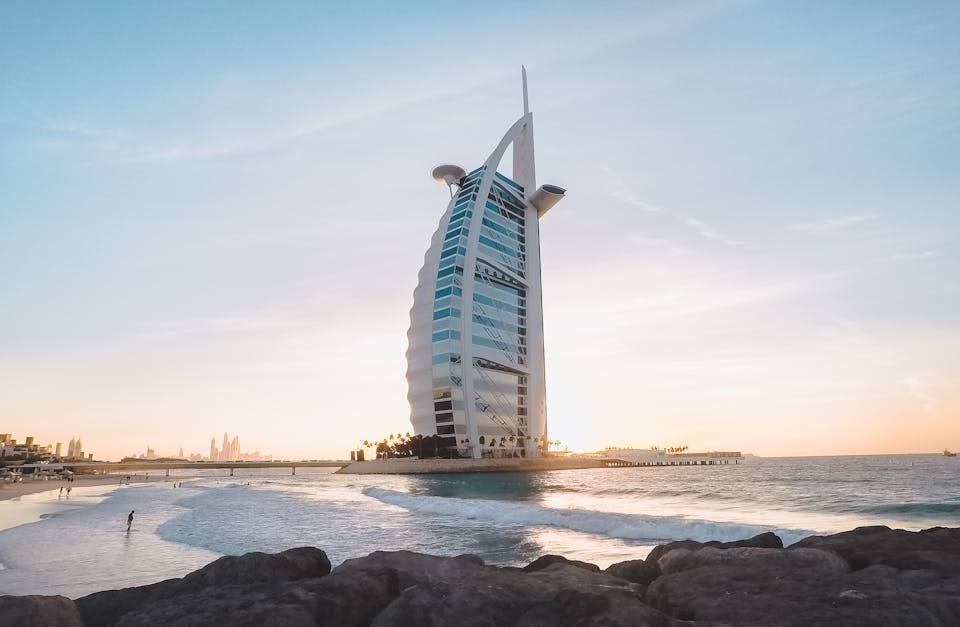 Burj Al Arab sail-shaped hotel at golden hour with rocky shore and waves in the foreground, Dubai