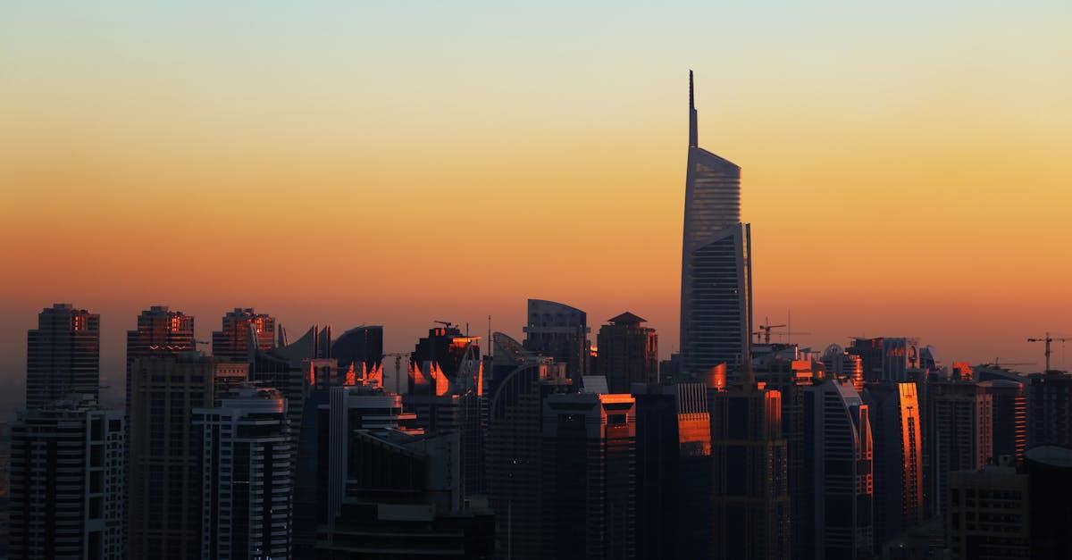 Dubai skyline silhouette at sunset with Almas Tower rising above the city under an orange sky