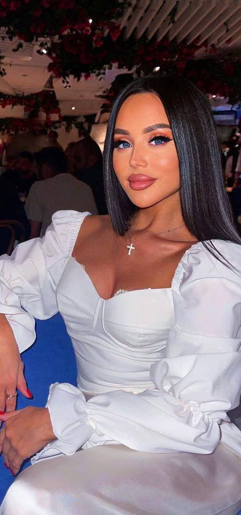 Woman with long dark hair in a white puff-sleeve corset top sitting in a restaurant decorated with red flowers