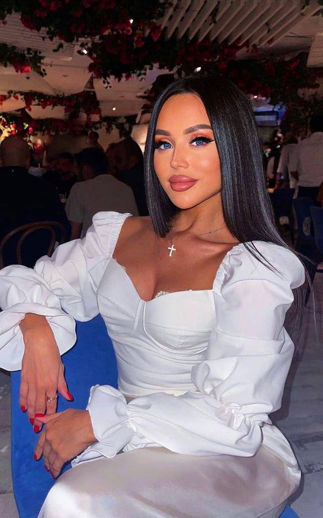 Woman with long dark hair in a white puff-sleeve corset top sitting in a restaurant decorated with red flowers
