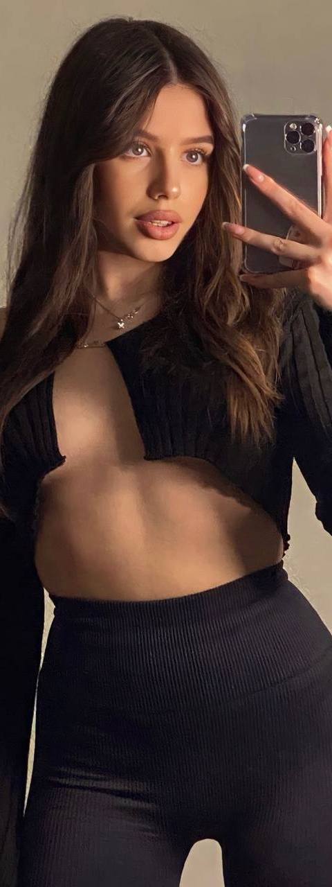 Mirror selfie of a brunette woman in a black off-shoulder ultra-cropped knit top and high-waisted leggings against a beige wall